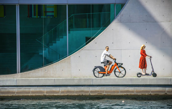 Two people with drive electric vehicles in front of the Federal Chancellery along the river Spree