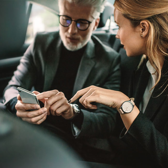 Geschäftsmann und -frau sitzen in einem Auto schauen auf ein Smartphone und diskutieren