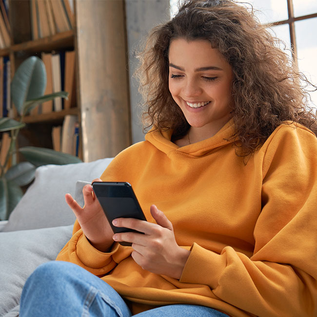 Satisfied woman sitting at home on sofa and looking at her smartphone