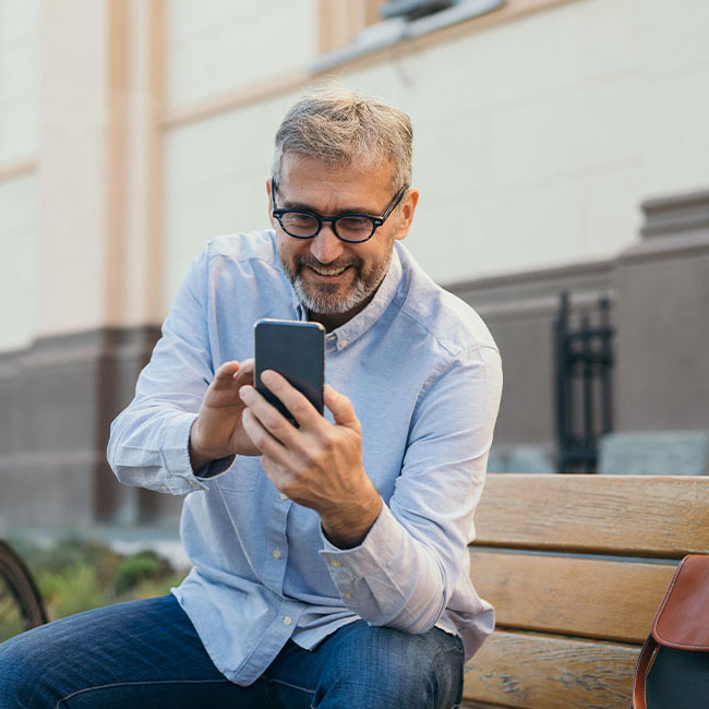 Mann sitzt mit Smartphone in der Hand auf einer Bank und lächelt