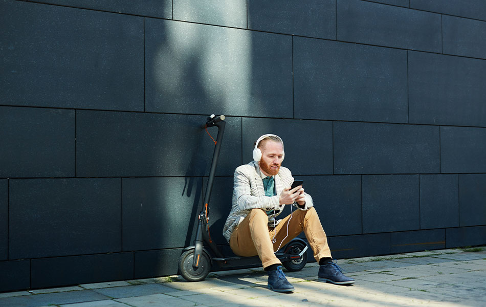 Mann sitzt auf e-Scooter vor einer Wand und schaut auf sein Smartphone